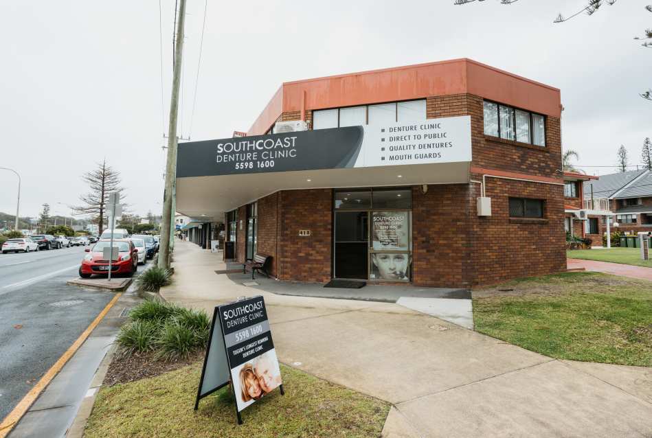 A charming brick denture clinic on the Gold Coast features a sidewalk sign proudly advertising services, contact details, and expertise in crafting false teeth.
