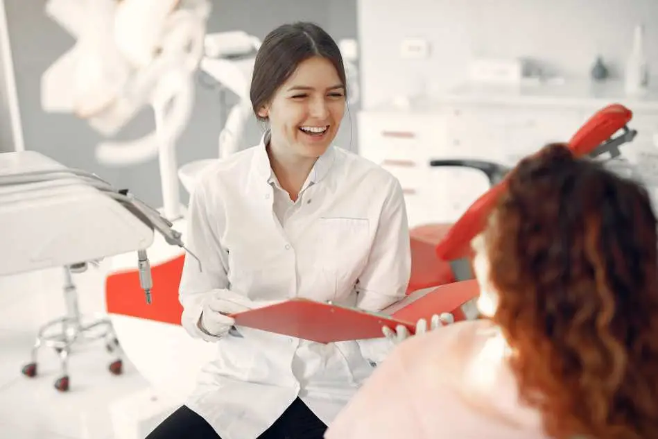 Dentist smiling at patient in a denture clinic, holding a red clipboard.