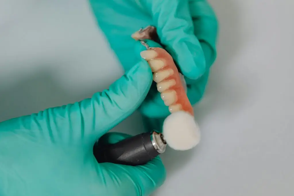 Gloved hands are expertly polishing dentures with a dental tool, ensuring they gleam like those crafted at a Gold Coast denture clinic.
