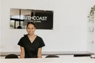 Person in black scrubs at a reception desk with "Southcoast Denture Clinic" sign behind.