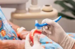 Gloved hands holding dentures and a toothbrush in a dental setting.
