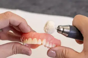 Hands cleaning dentures with a polishing tool.