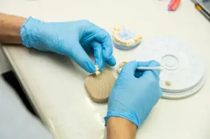 Person with blue gloves crafting dental prosthetic with tools on a table.