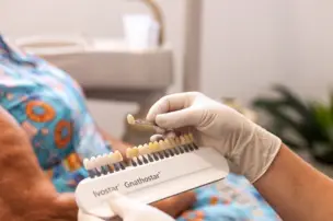 A dentist selects a tooth color using a shade guide for a patient in a dental office.
