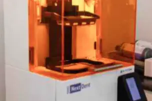 3D printer with an orange cover and NextDent label on the front panel.