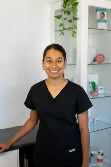 Person in black scrubs stands in a dental office, ready for denture repairs, with plants around.