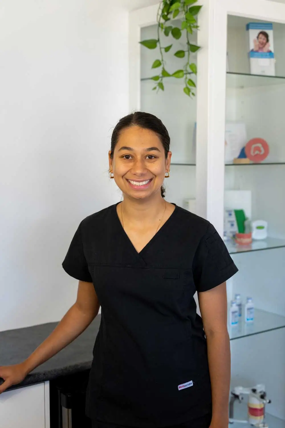 Person in black scrubs stands in a dental office, ready for denture repairs, with plants around.