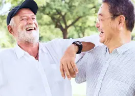 Two men, one wearing a cap and the other in glasses, are smiling and laughing outdoors near a denture clinic.