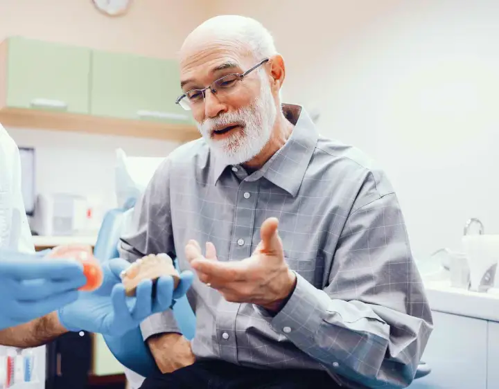A man discusses dental prosthetics with a dentist in a denture clinic office.