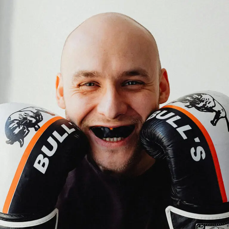 Person smiling with boxing gloves and a mouthguard, showcasing their confidence and readiness. Whether it's in the ring or just everyday life, having secure gold coast dentures ensures your smile is always at its best.