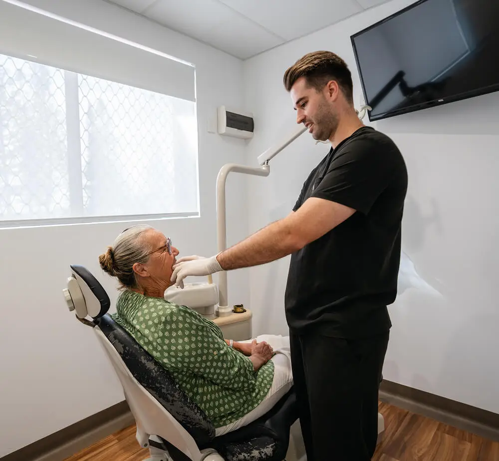 Dentist discusses denture implants with older woman seated in a dental chair at a modern clinic.