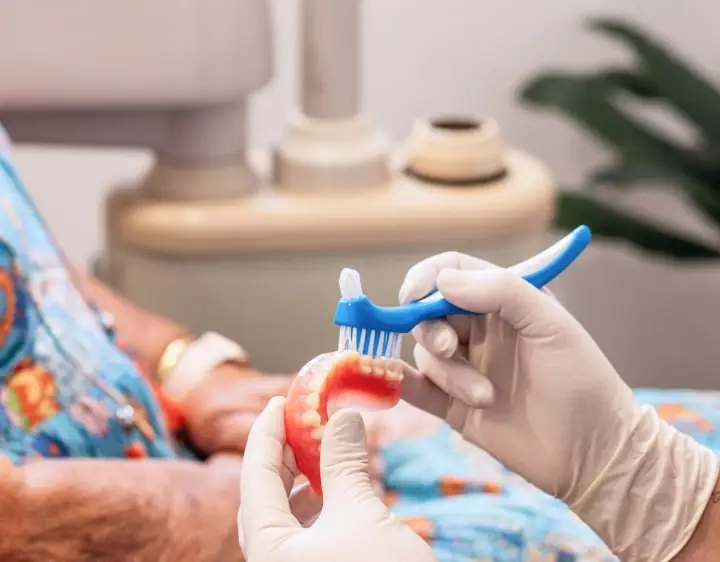 Gloved hands cleaning dentures with a toothbrush at a denture clinic.