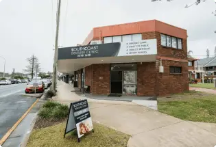 Street view of South Coast Dental Clinic, a charming brick building with signage, located in the heart of Palm Beach, specializing in high-quality dentures.