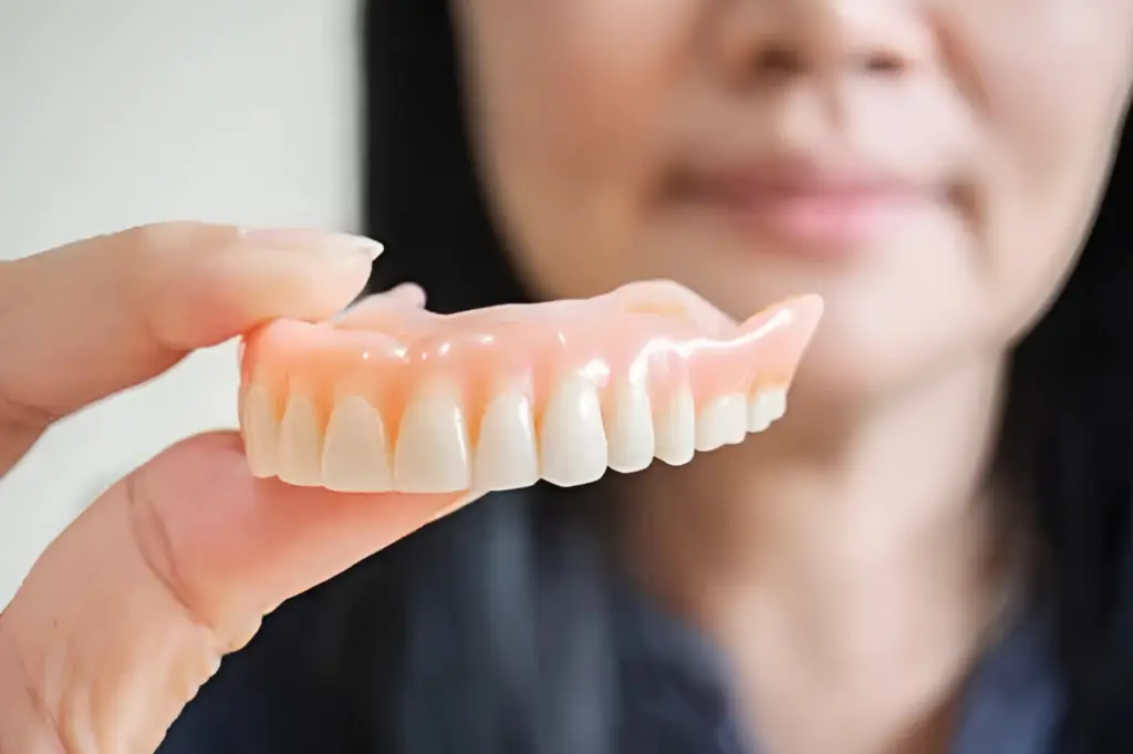 A person holding a set of dentures in their hand showcases everything you need to know about dentures.