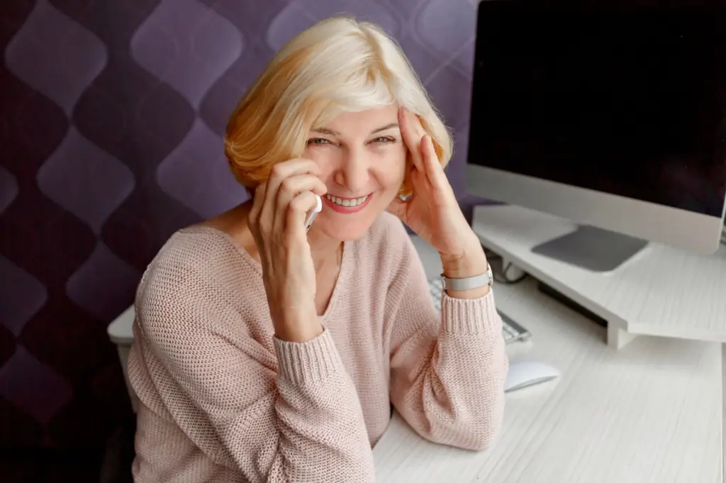Smiling woman, discussing partial dentures, sits at a desk with a computer.