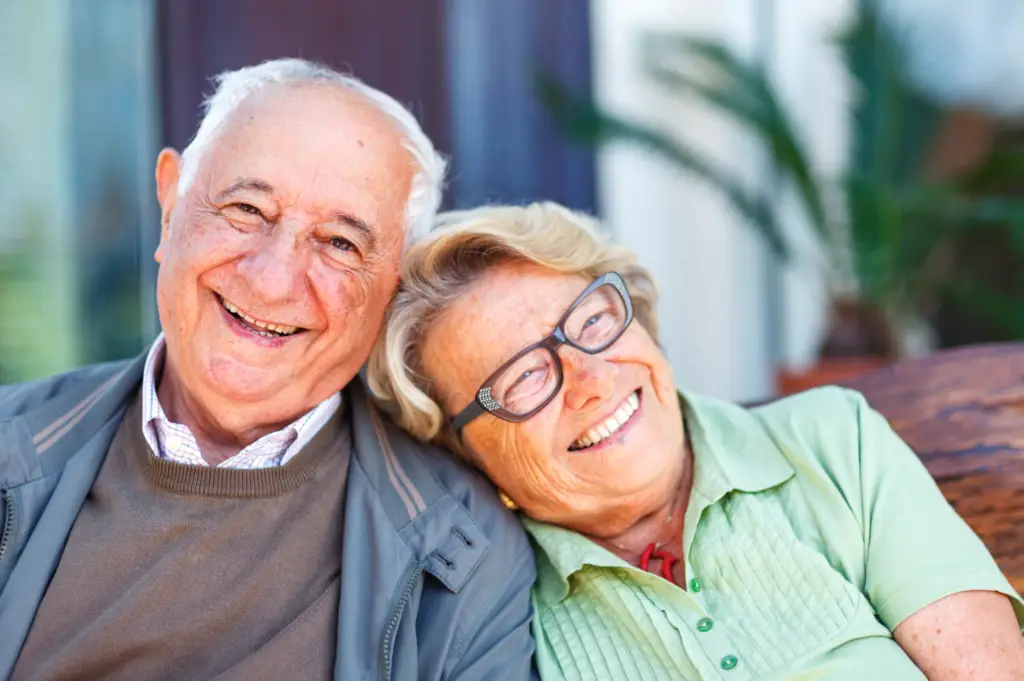 Elderly couple smiling together outdoors, sharing tips on caring for their new dentures.