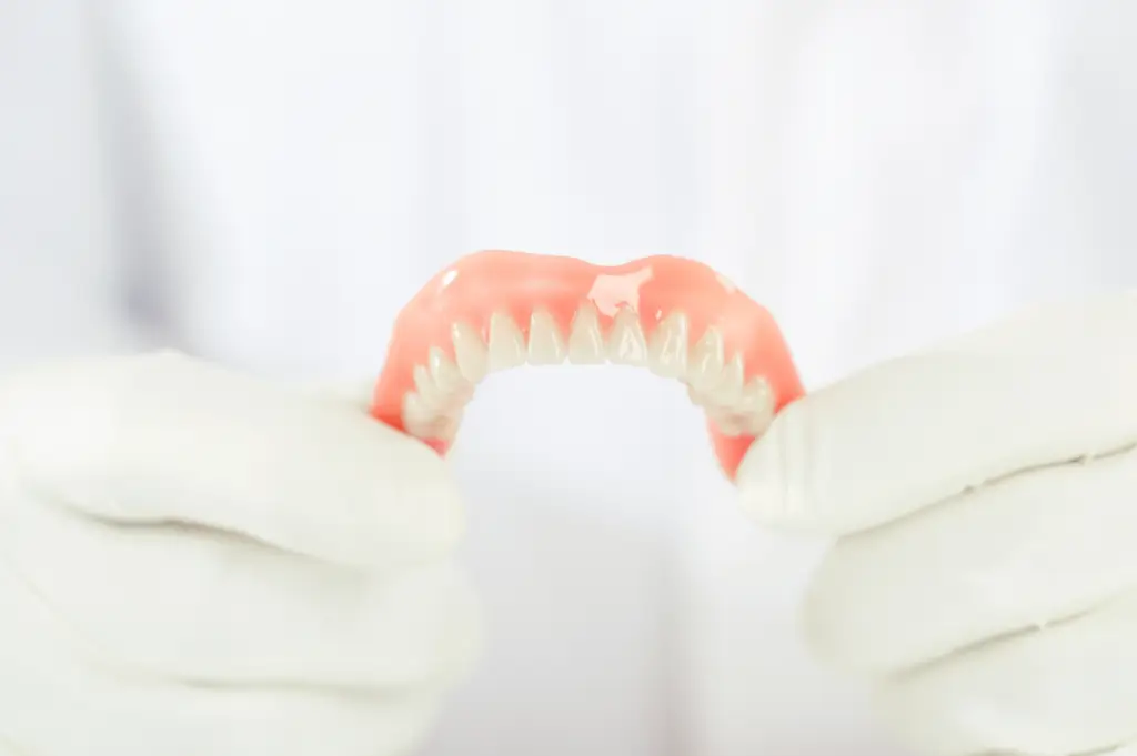Caring for your mouthguard, a person holds dental dentures with white-gloved hands.
