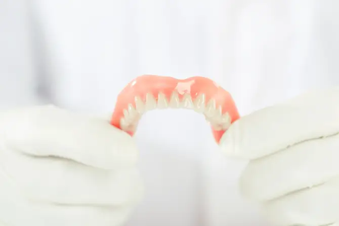 Caring for your mouthguard, a person holds dental dentures with white-gloved hands.