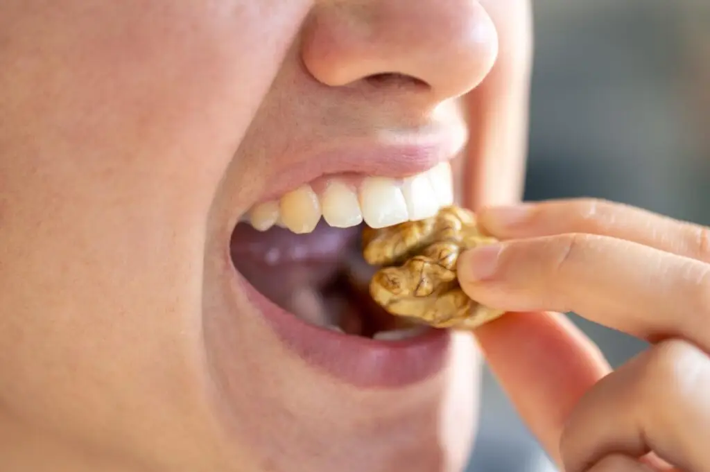 Person biting a whole walnut with their dentures..
