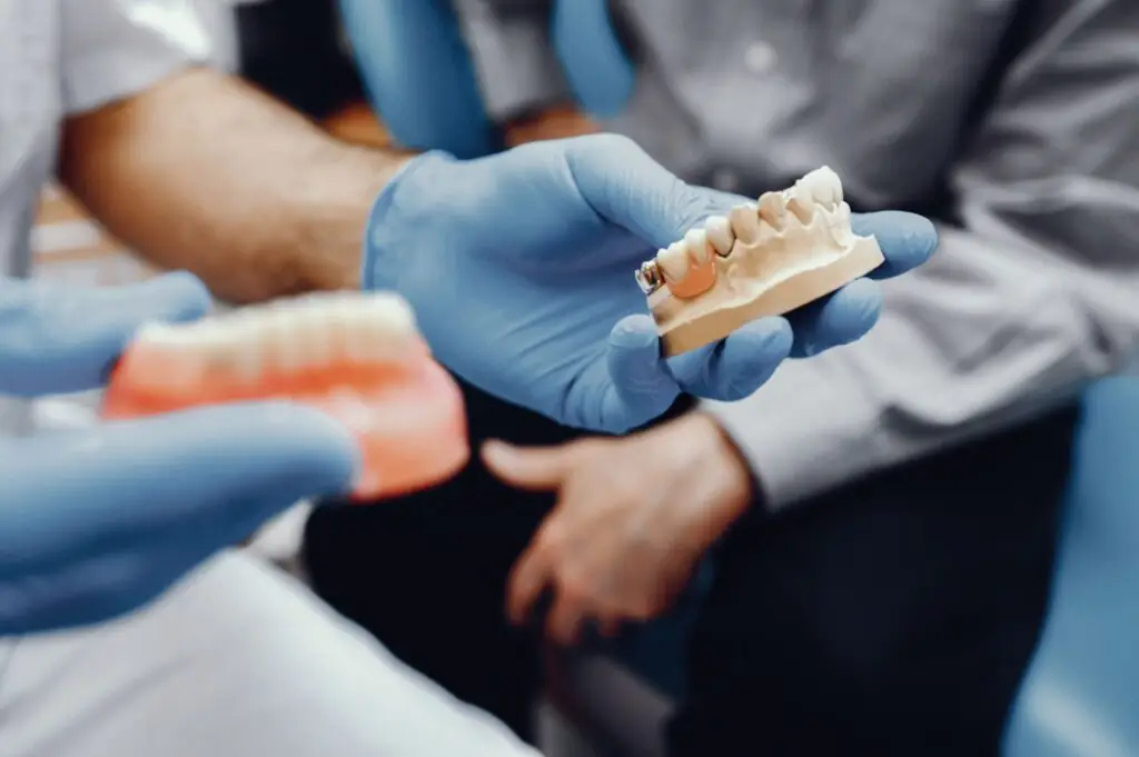 Gloved hands showcase dental models highlighting the benefits of dentures versus implants.