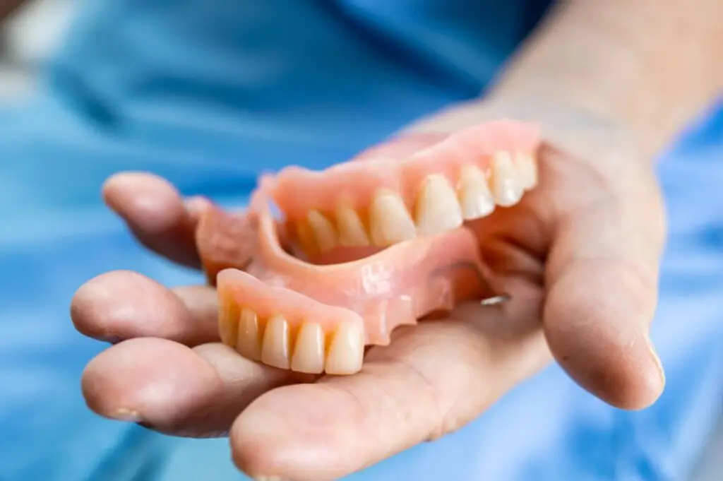 A close-up of a hand holding a set of dentures, highlighting different materials used in denture construction