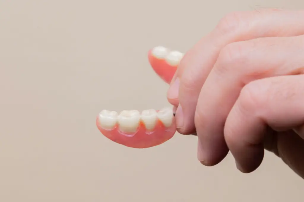 Hand holding implant-supported dentures against a plain background.