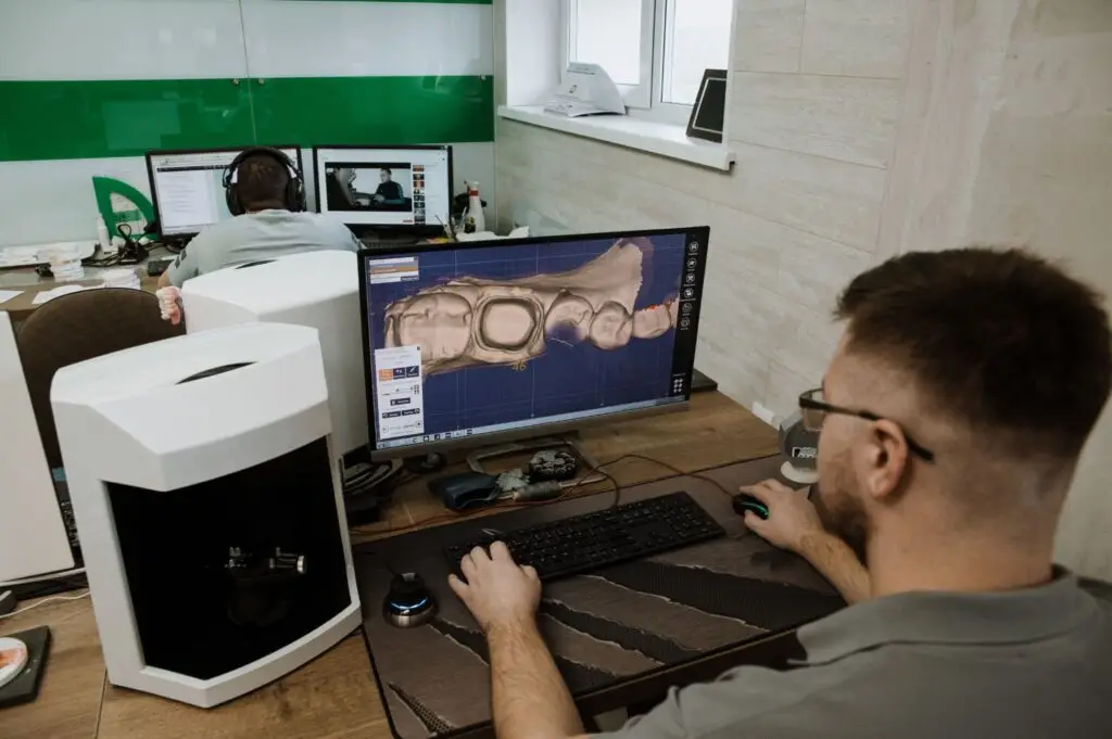 A man designs complete dentures vs dental implants using 3D modeling software in an office.