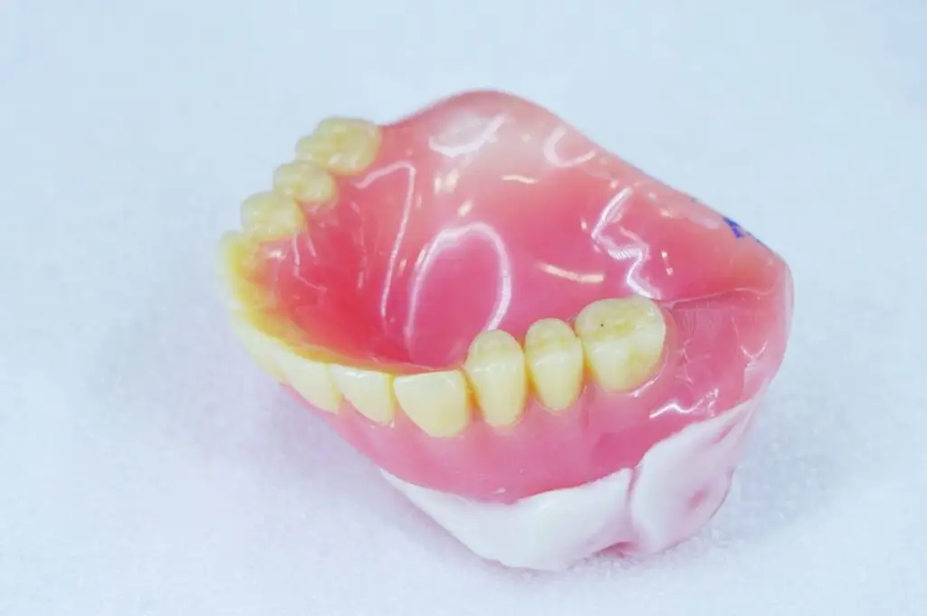 A set of upper dentures from a Denture Clinic with yellowed teeth on a white surface.