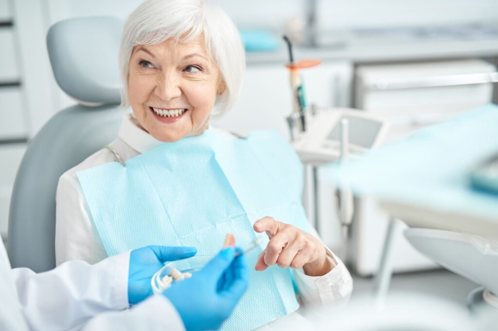 Elderly woman smiling in a denture clinic as a dentist shows her dental tools.