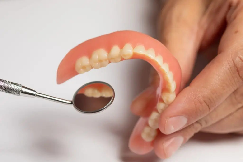 A person holds a tooth with a dental tool, illustrating the impact of dentures on jaw bone health.