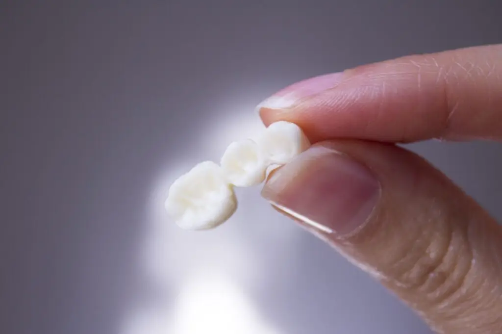 Someone holds a tooth with a toothbrush, showing how to care for partial dentures to ensure comfort and longevity.