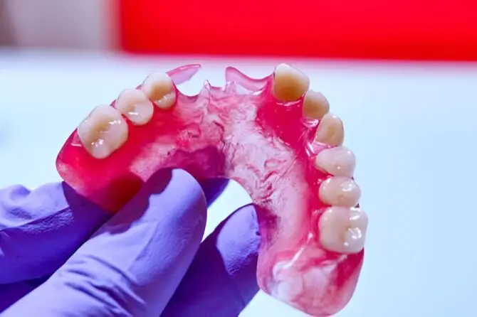 Gloved hand holding a pink partial denture, illustrating complete denture care.