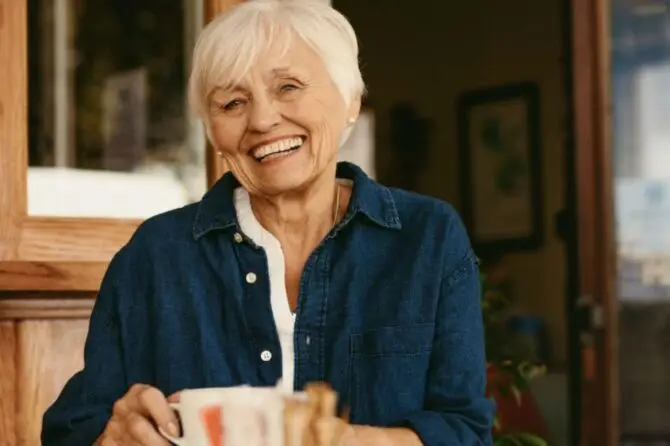 A senior woman at a table with a coffee cup, contemplating the pros and cons of immediate vs. conventional dentures.