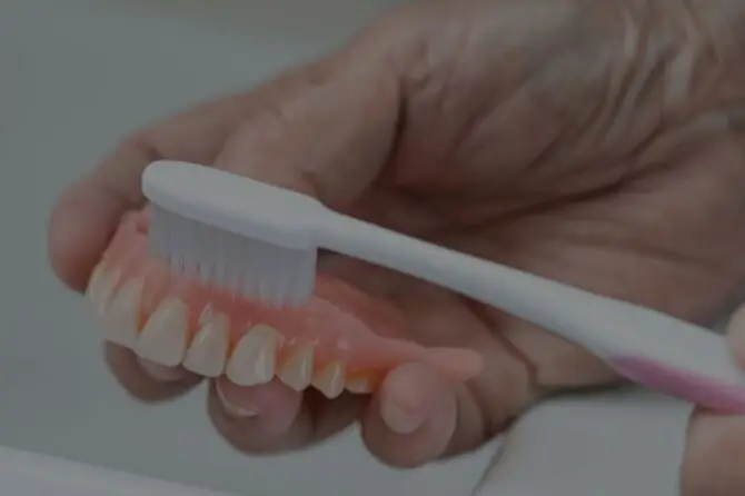 A person using a toothbrush to clean their dentures, highlighting denture care during the healing process.