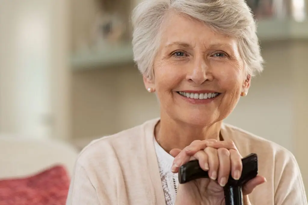 Older woman smiling indoors, hands on cane, showing confidence from proper denture care.