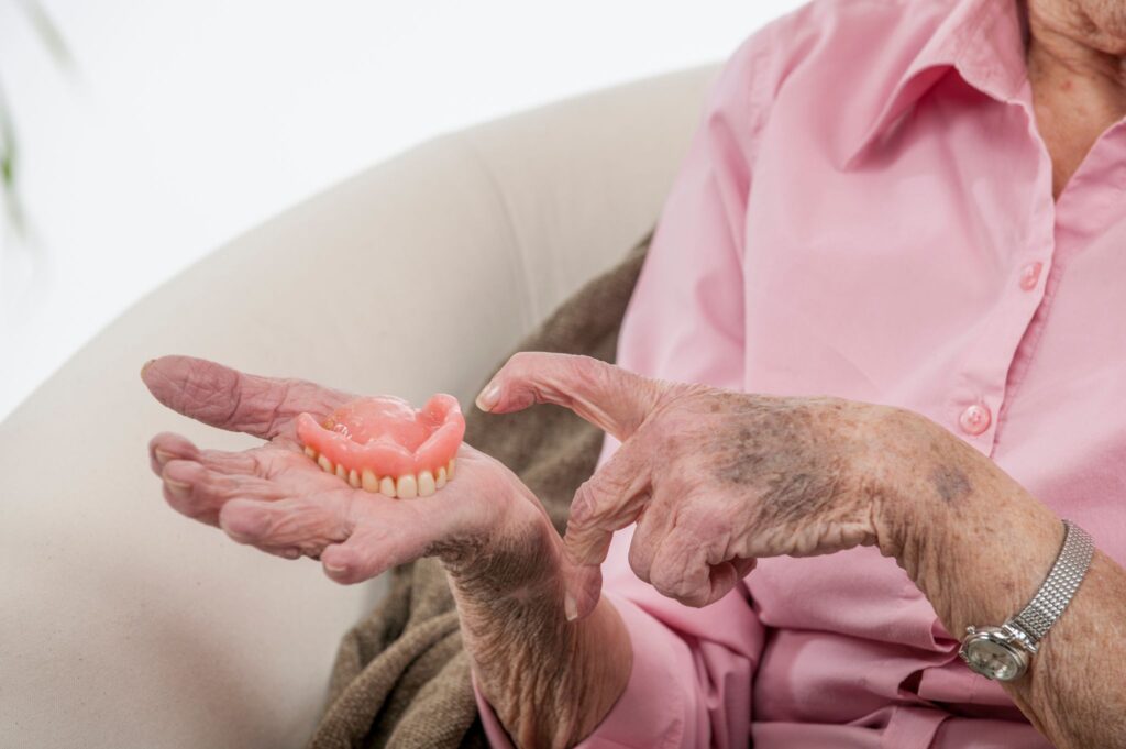 An elderly person points at dentures, perhaps wondering why dentures become loose over time.