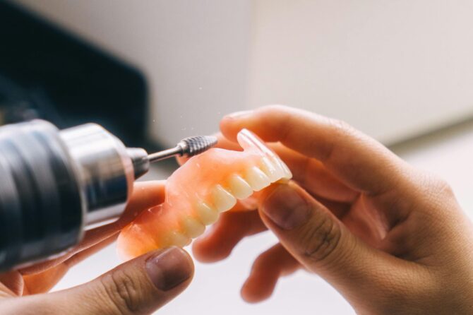 Person polishing a set of dentures with a dental tool, highlighting denture relines cost in Australia.