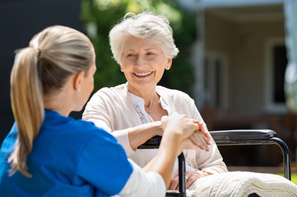 Nurse holding hands with smiling elderly woman learning if pensioners get help paying for dentures.