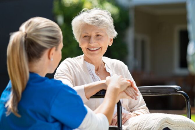 Nurse holding hands with smiling elderly woman learning if pensioners get help paying for dentures.